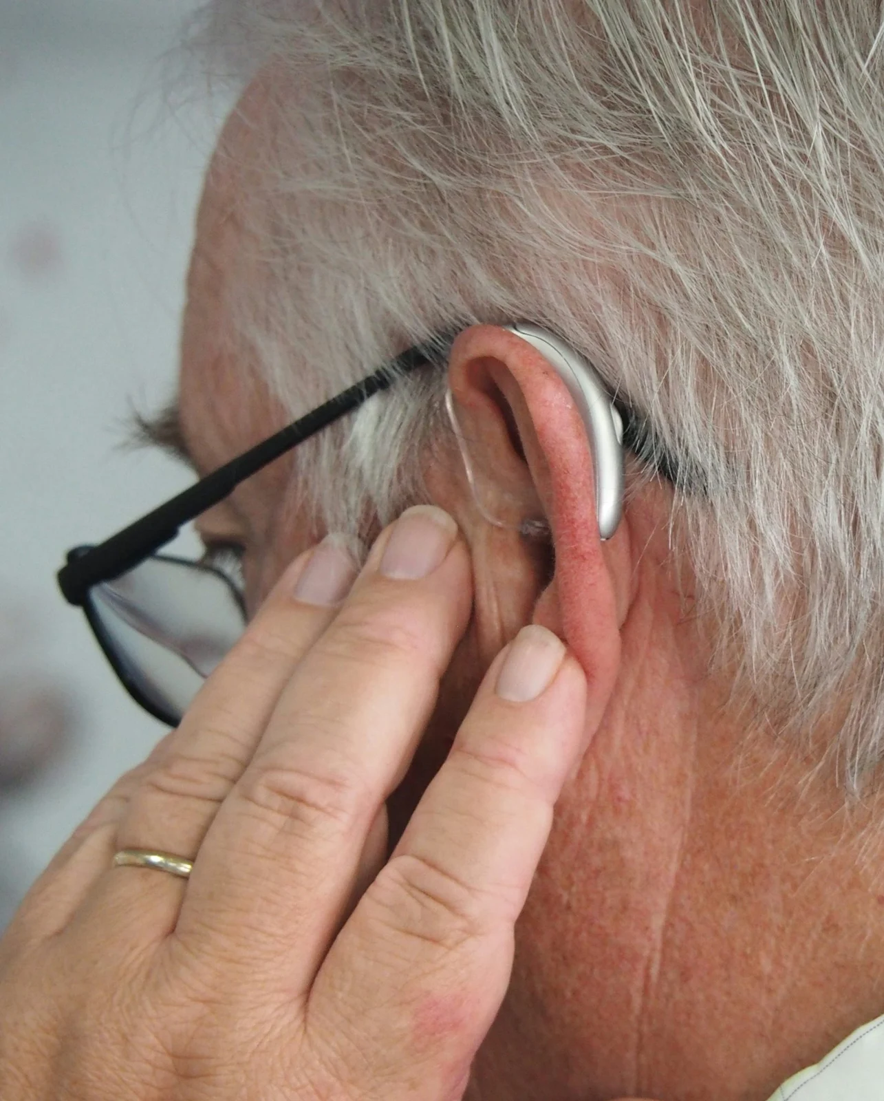 Mann mit Brille und einem silbernen Hörgerät hinter dem Ohr